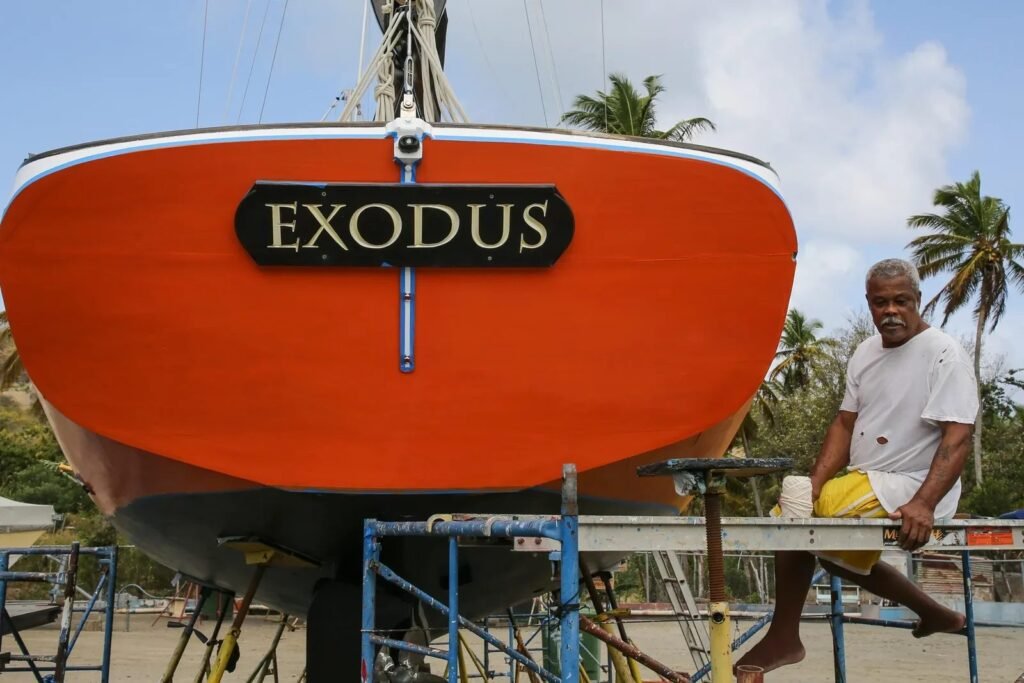 La coque rouge du Carriacou sloop Exodus sur son ber, avec un charpentier à Carriacou