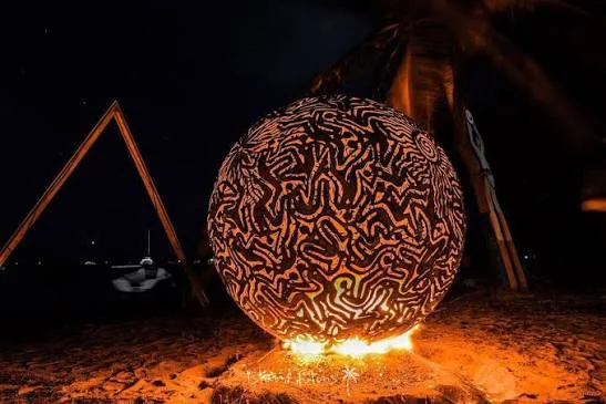 Une sculpture de feu sphérique d’Aragorn Dick-Read allumée la nuit sur la plage de Trellis Bay