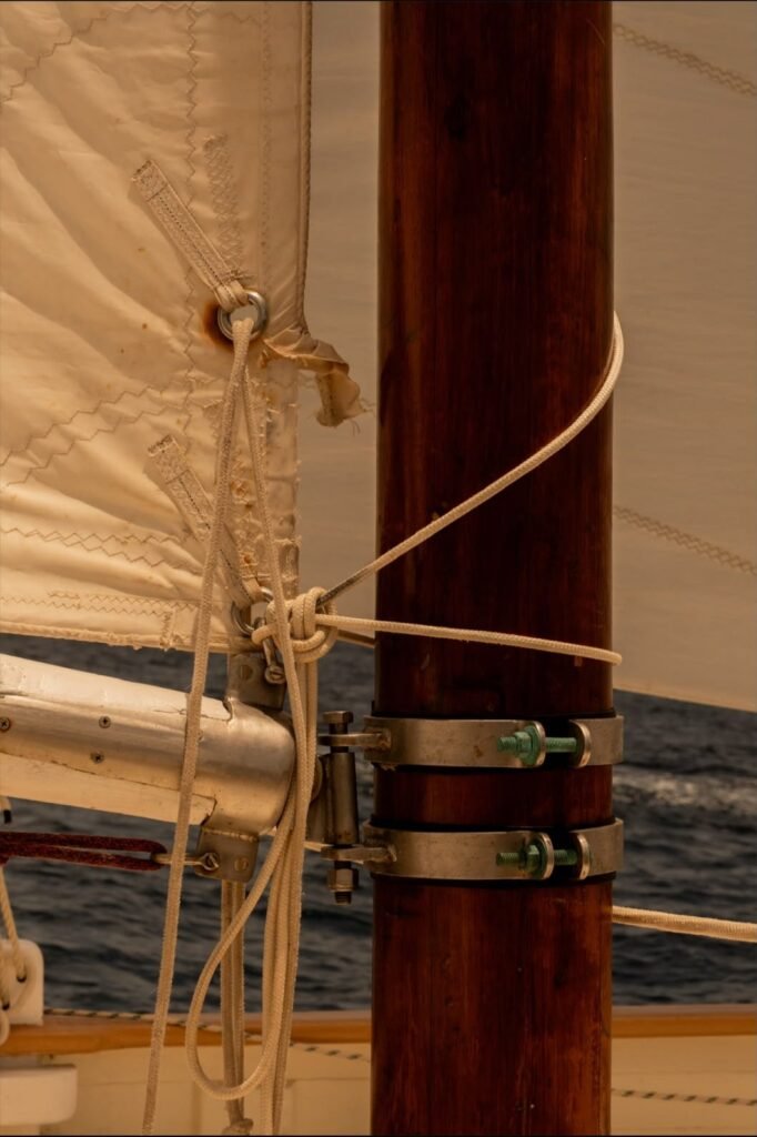 Gros plan sur le mât en bois verni d'un sloop traditionnel caribéen : colliers de fixation de la corne, cordages en fibre et voile cousue main, en navigation.