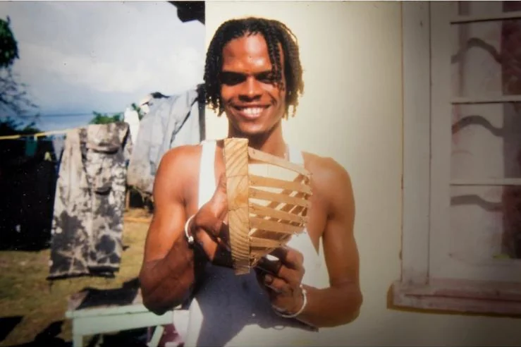 Le jeune Callistus Enoe, souriant, tient la maquette de Genesis taillée par son père