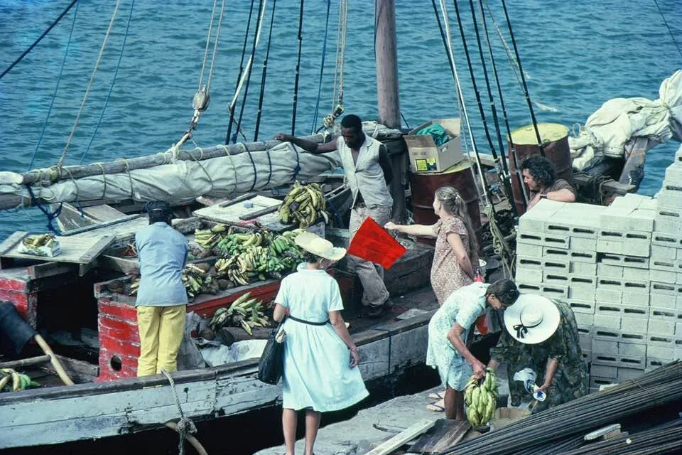 Régimes de bananes débarqués d’un sloop au quai de Gustavia, des clients autour des caisses