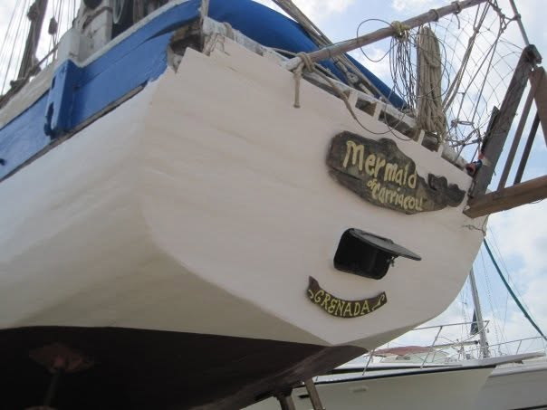Le tableau arrière du sloop, coque blanche fraîchement peinte, portant le nom sculpté et doré « Mermaid of Carriacou » et la plaque « Grenada »