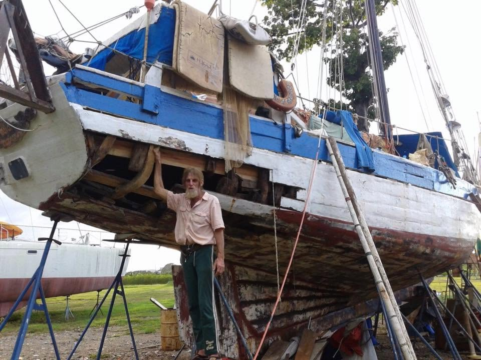 Le sloop Mermaid au sec, un pan de bordé déposé laissant voir les membrures, son capitaine debout contre la coque