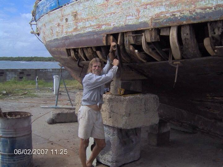 Le capitaine du Mermaid sous la coque calée sur des plots de béton, membrures et boulons de quille apparents