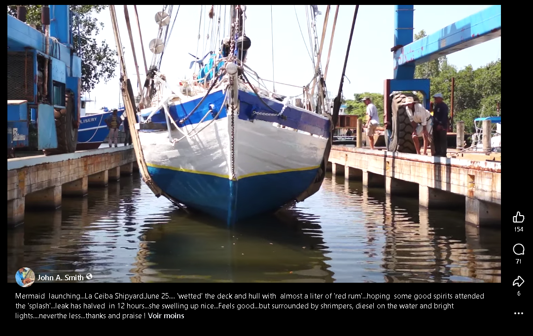 Le sloop Mermaid à flot entre deux quais du chantier de La Ceiba au Honduras, coque blanche et bleue fraîchement peinte, quelques hommes sur le ponton
