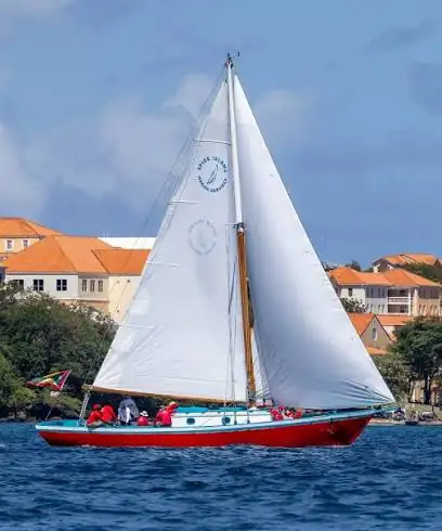 Le sloop Savvy, coque rouge, sous voiles au large de la Grenade, le logo de la West Indies Regatta sur la grand-voile