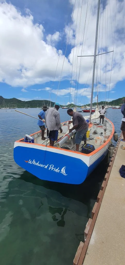 Le sloop Windward Pride à quai, coque bleue et blanche, équipage à bord en plein préparatifs
