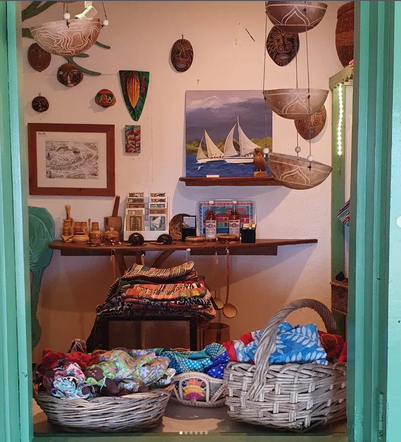 L’intérieur de la boutique d’Aragorn : masques et calebasses sculptés aux murs, tableau de deux voiliers, tissus colorés dans des paniers en osier